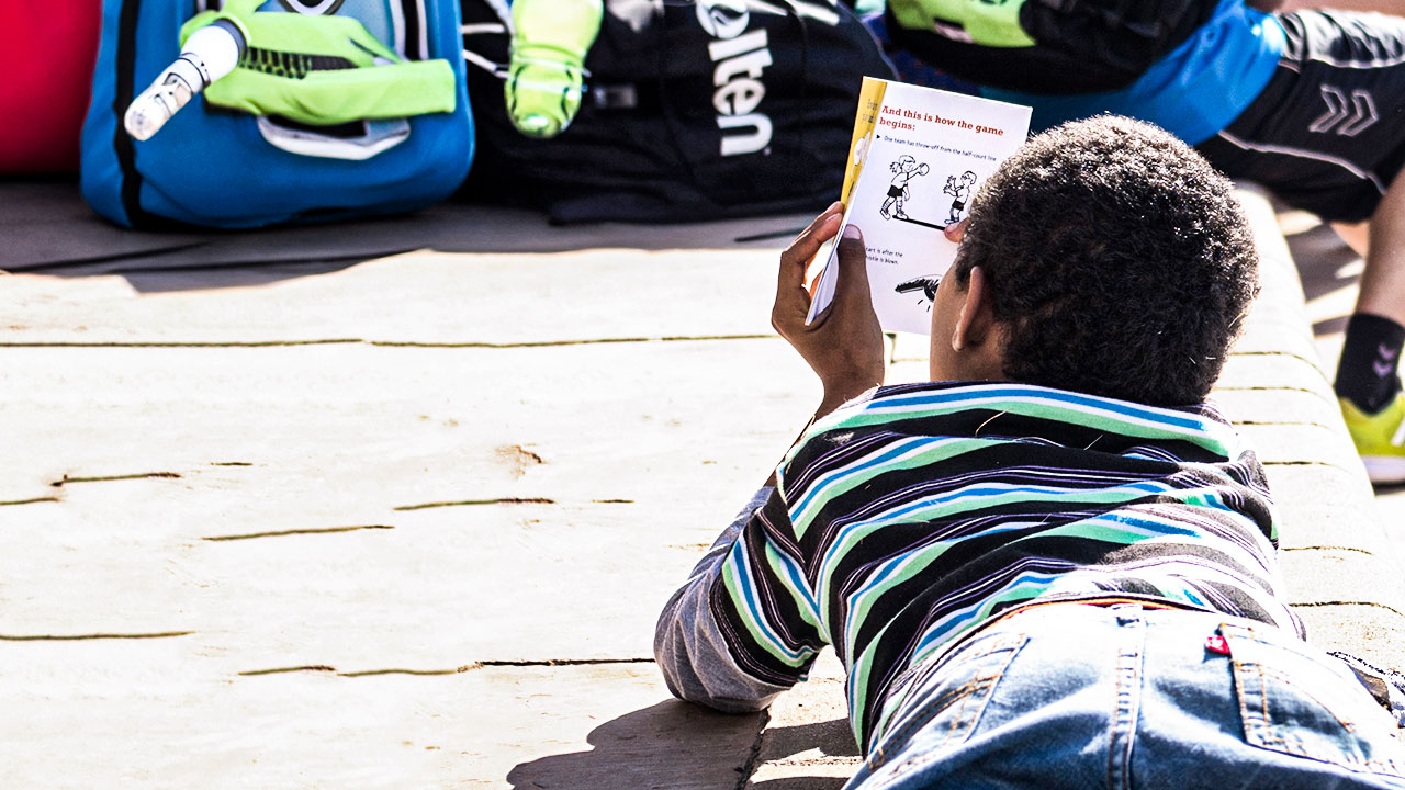 A little boy is lying on the floor, attentively reading a manual describing various sports exercises.