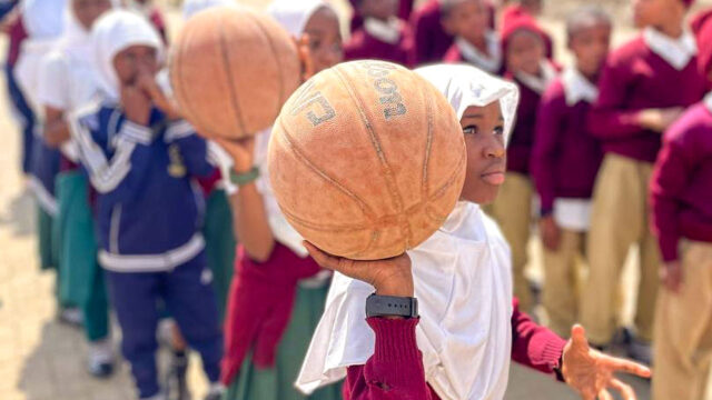 A girl wearing a headscarf from Tanzania proudly holds up a basketball during training.