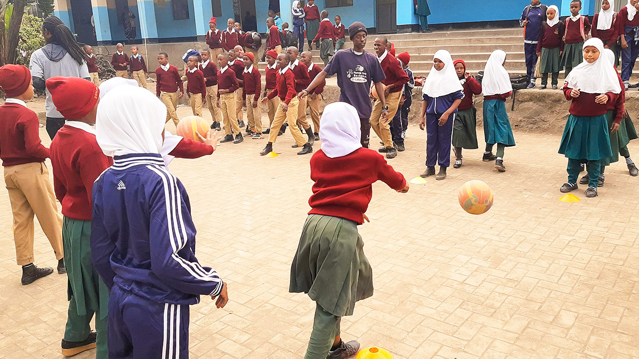 Mädchen in Schuluniformen stehen sich gegenüber und werfen sich Basketbälle zu.