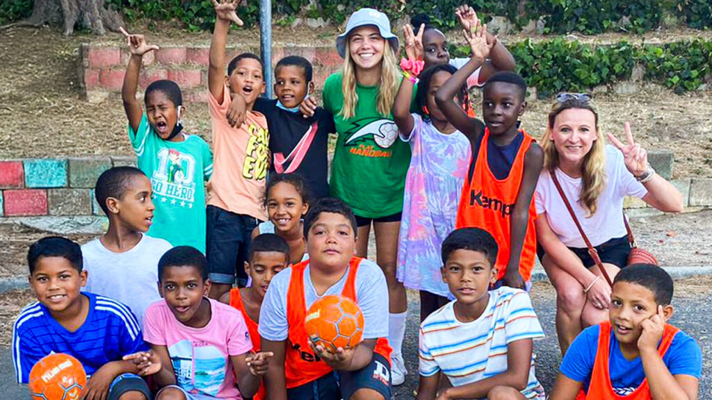 Zwei Sporttrainerinnen beim Freiwilligendienst im Ausland posieren für ein Mannschaftsfoto zusammen mit Kindern ihrer Mannschaft in Kapstadt.