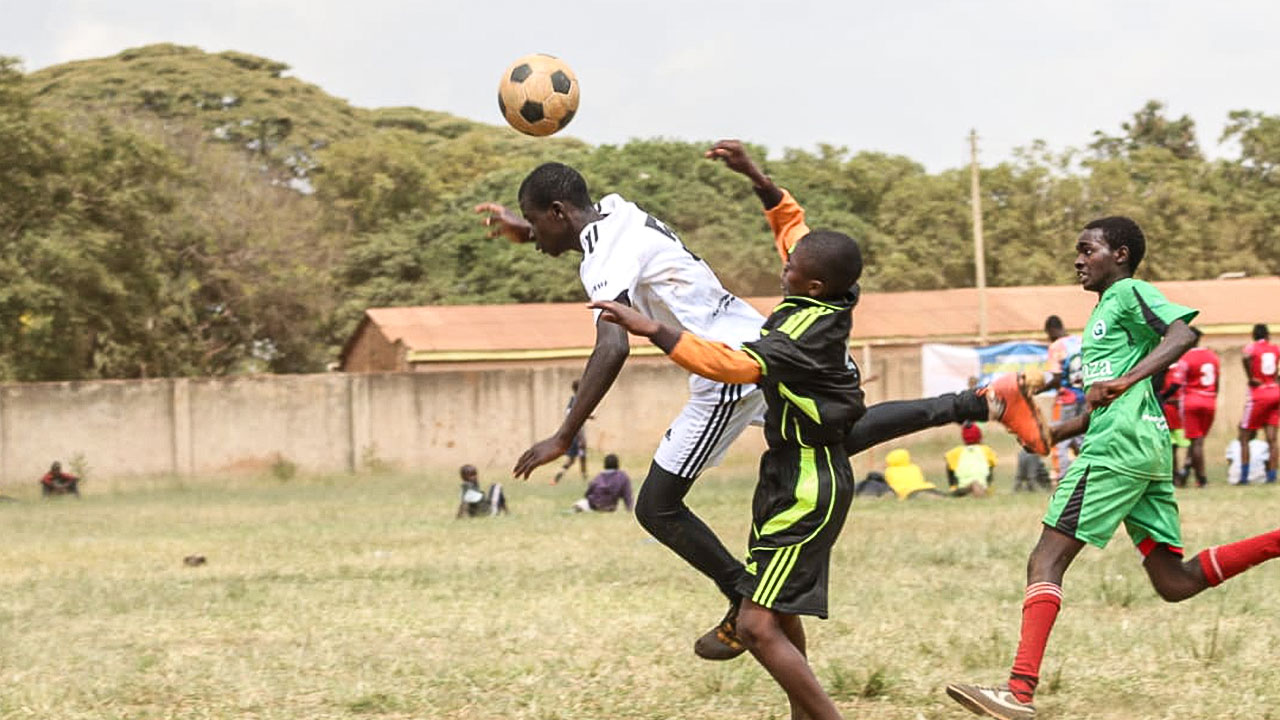 Football scene with three players from the Football for a Good project jumping for a header.