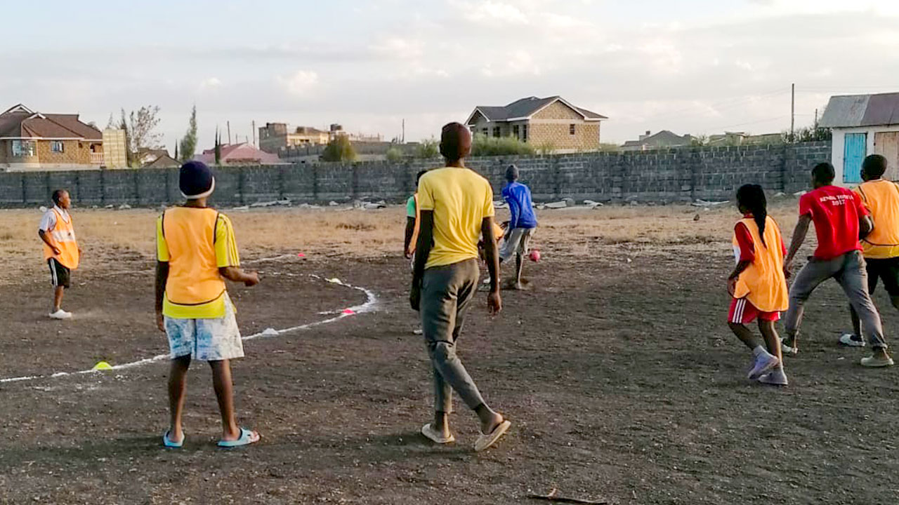 Eine Gruppe von Kindern und Jugendlichen in Badelatschen trainiert in einem Wohngebiet auf einer Freifläche mit holprigem und steinigem Untergrund Handball.