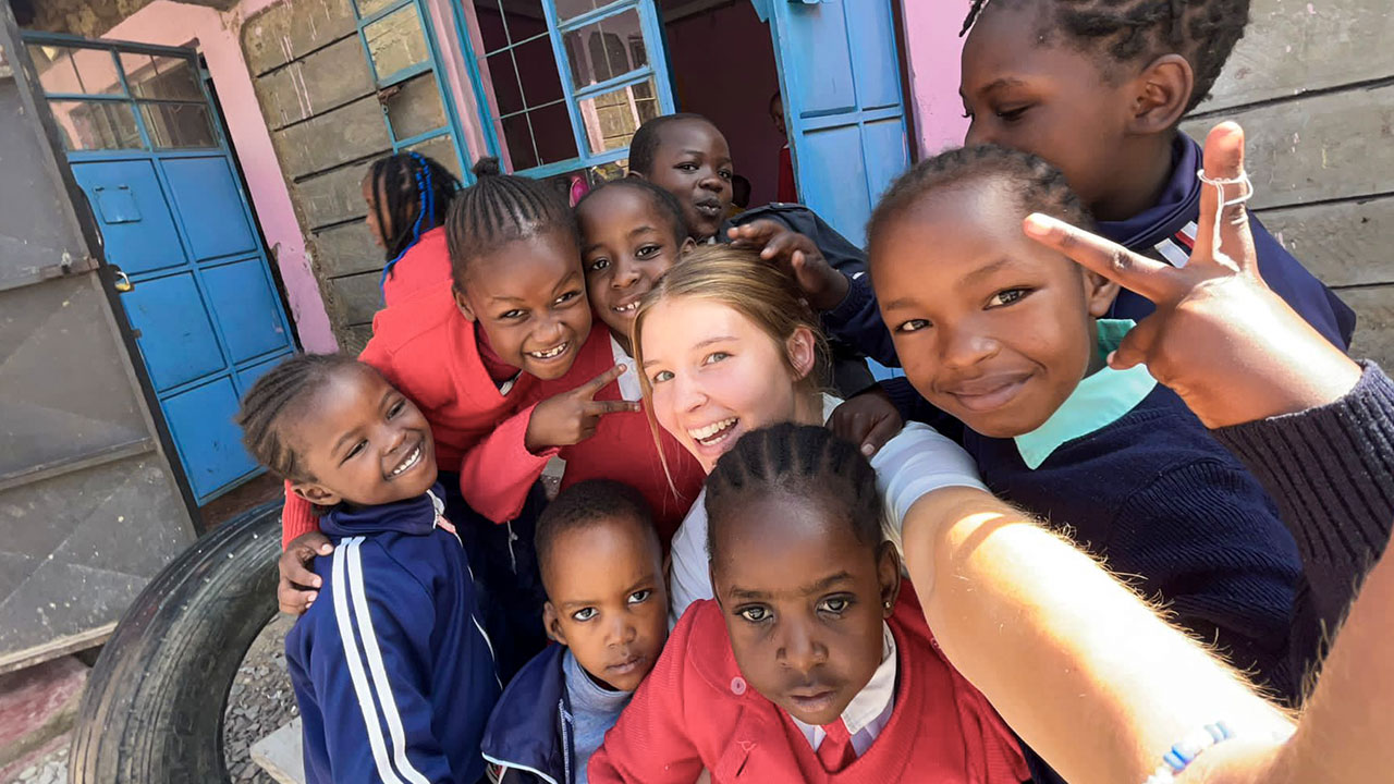 Umringt von lachenden Kindern aus ihrem Sportprojekt macht eine freiwillige Sporttrainerin ein Selfie.