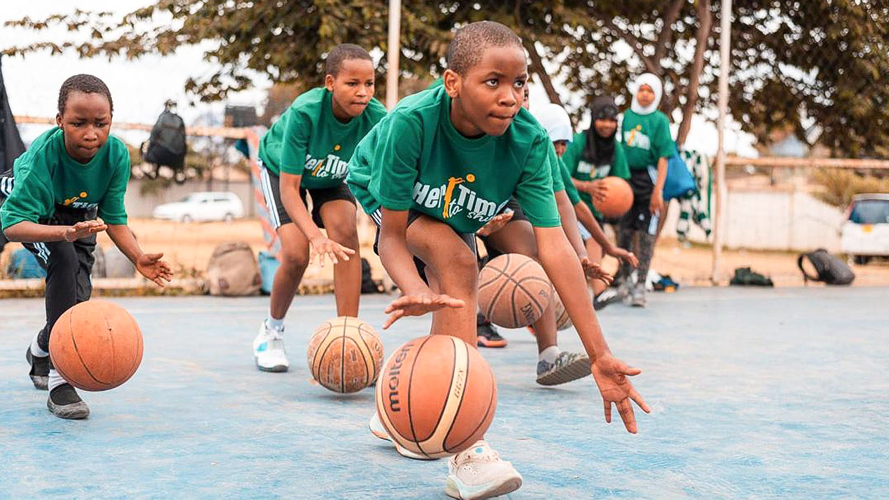 Beim Basketballtraining dribbeln Jungen und Mädchen in hockender Pose.