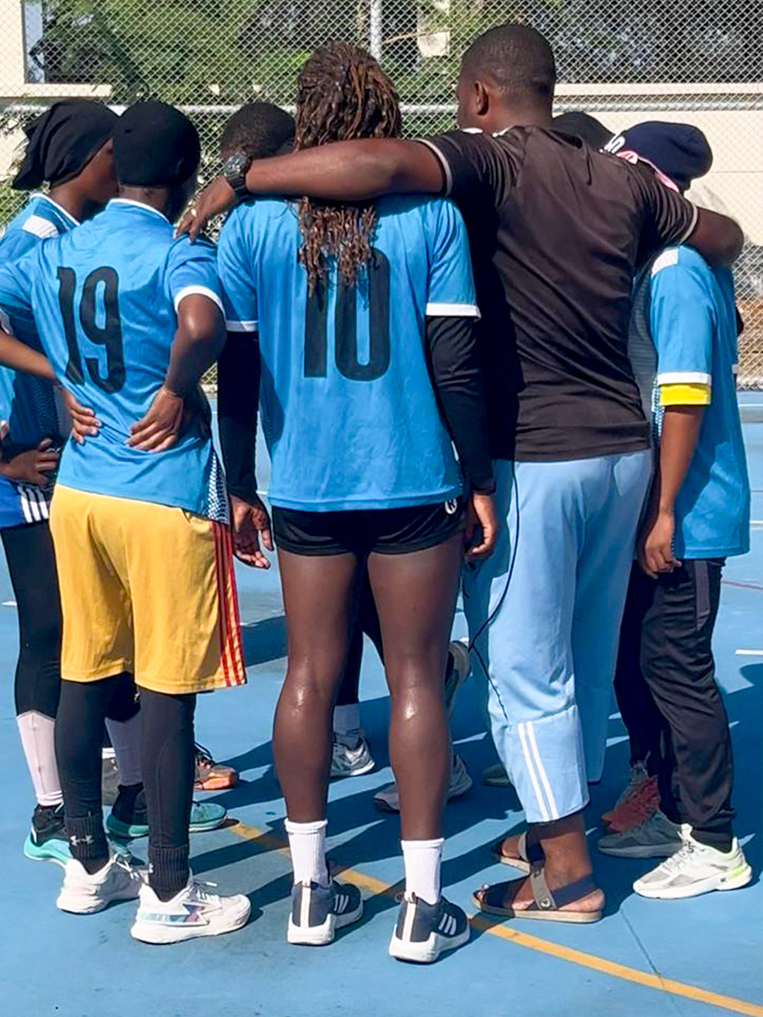 The handball team stands arm in arm in a circle, motivating one another before training or a match.