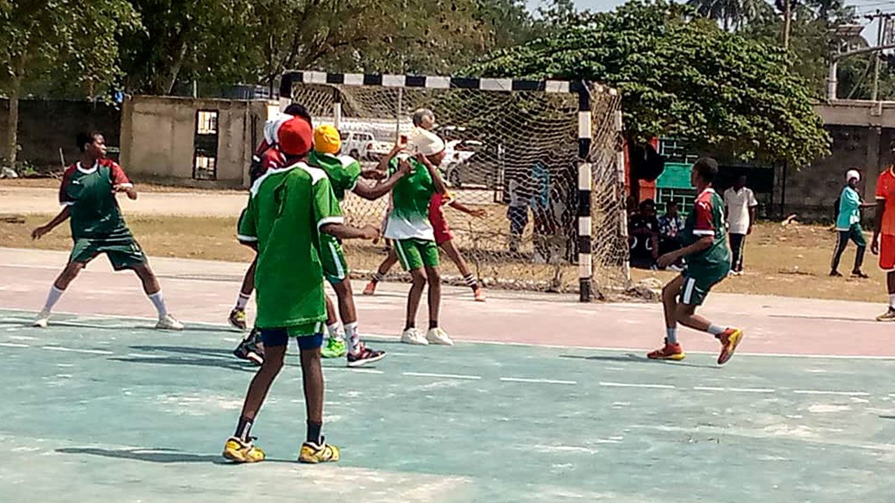 A mixed boys' and girls' team attacking their opponents' handball goal on the school's green, concrete sports field.