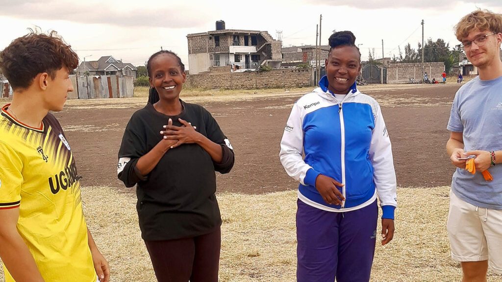 Mentorinnen von „PLAY HANDBALL Kenia” unterhalten sich auf einem Spielfeld mit freiwilligen Sporttrainern aus Deutschland.